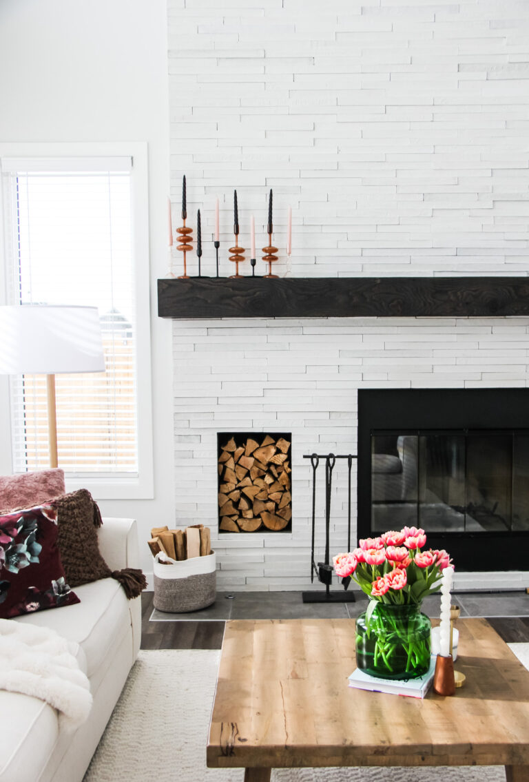 a living room with a white stone fireplace, white couch and wooden table with a bouquet of tulips