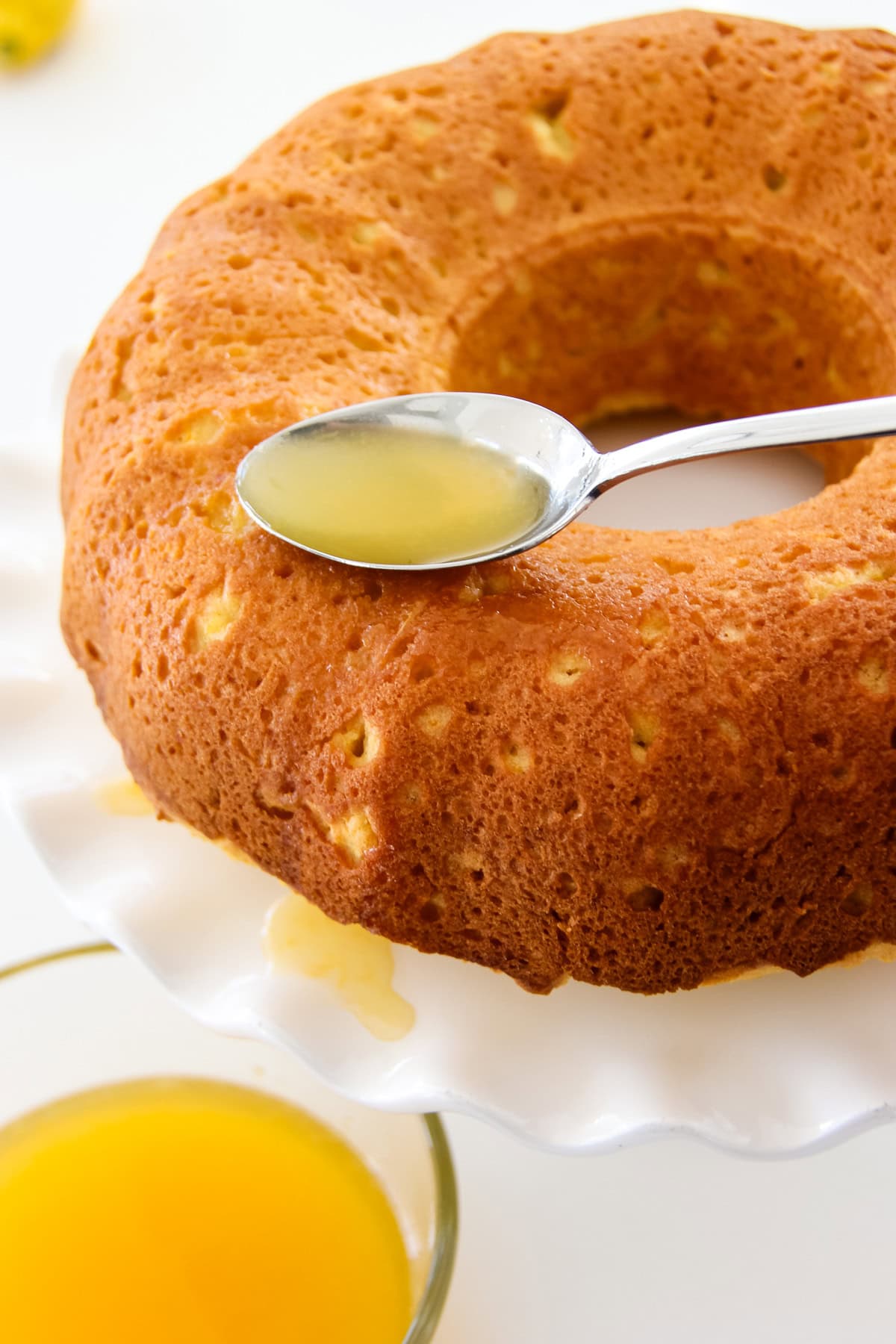 a spoon of orange juice being drizzled onto an orange bundt cake