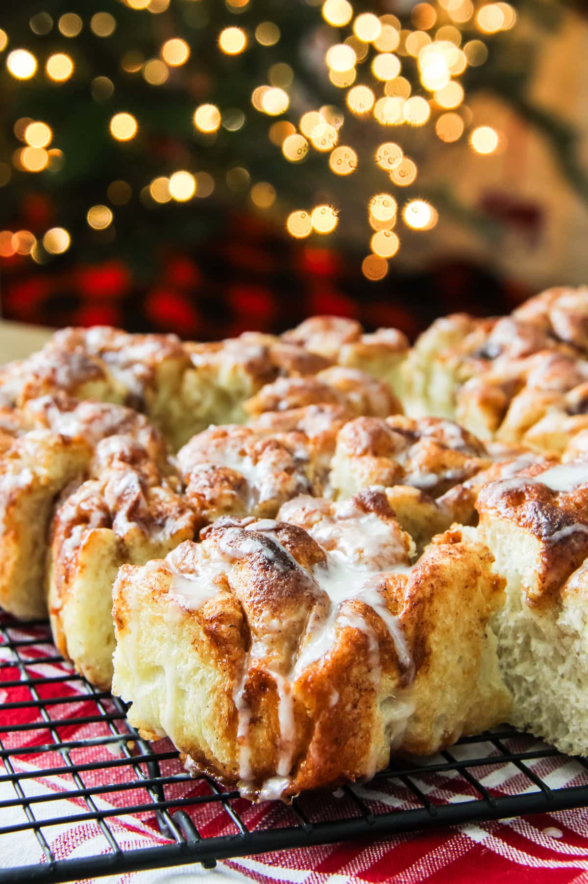 squares of cinnamon roll focaccia on a wire cooling rack. Christmas tree lights are twinkling in the background