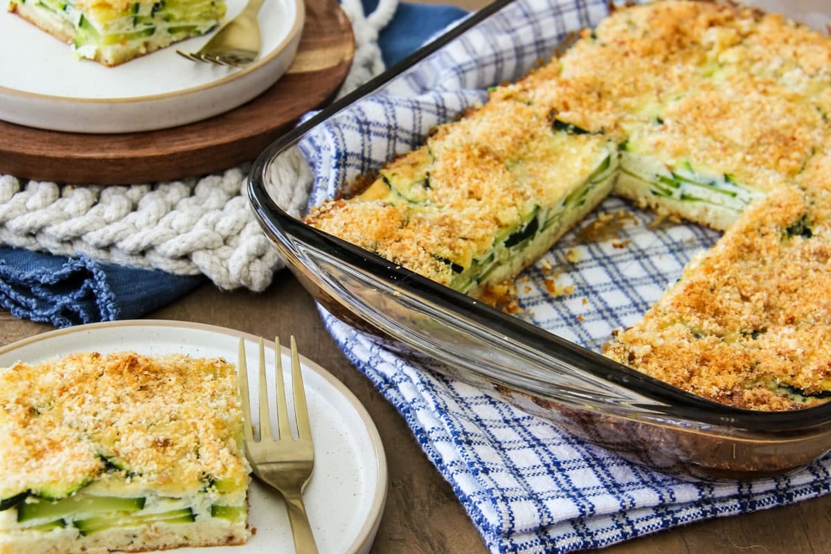 a slice of crustless zucchini pie on a plate, next to a pan of zucchini pie