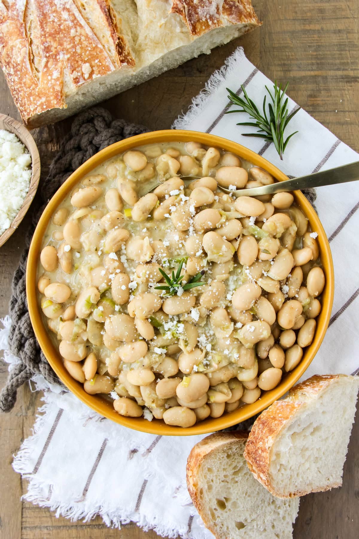 a top down image of a bowl of Rosemary Garlic Butter Beans next to sourdough bread